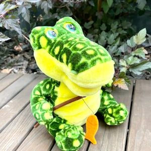 May include: A green and yellow plush crocodile toy with a fishing rod and a fish. The crocodile has a spotted pattern and big green eyes.