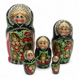 Könnte beinhalten: Ein Set aus fünf russischen Matrjoschka-Puppen in verschiedenen Größen. Jede Puppe hat eine schwarze Basis mit floralen und blattartigen Designs in Rot, Grün und Gold. Die Puppen haben bemalte Gesichter mit rosigen Wangen und goldenen Akzenten.