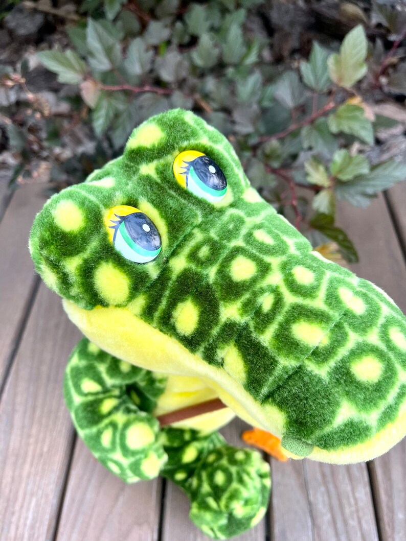 May include: Green and yellow plush alligator toy with large, round eyes. The alligator has a textured, spotted pattern.