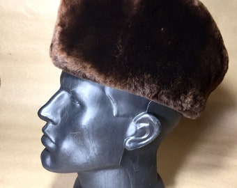 May include: A brown faux fur hat with a square crown and a wide brim.