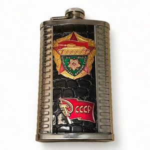 May include: A silver flask with a black crocodile-embossed design. It features a red, gold, and green enamel emblem with a tank and the text "1941-1945", "БРОНЕТАНКИ", and "В РУКАХ СССР". There is also a red and gold enamel emblem with a hammer and sickle and the text "СССР".
