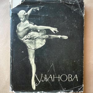Może przedstawiać: Okładka starej książki z czarno-białym zdjęciem baletnicy w wdzięcznej pozie. Baletnica ma na sobie zwiewną spódnicę na ciemnym tle. Tytuł "Ulanova" jest wydrukowany białą czcionką.