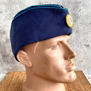 May include: A dark blue military style hat with a teal trim and a gold star emblem. The hat is worn on a mannequin head.