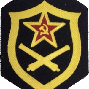 May include: A black felt patch with a gold border and a red star with a hammer and sickle inside. Two crossed gold cannons are below the star.