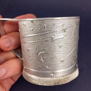 Peut inclure: Une tasse en m&eacute;tal argent&eacute; avec un motif d'&eacute;toile et de croissant de lune. La tasse a une poign&eacute;e et une surface textur&eacute;e.
