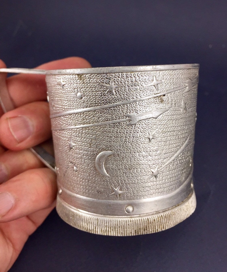 Peut inclure: Une tasse en m&eacute;tal argent&eacute; avec un motif d'&eacute;toile et de croissant de lune. La tasse a une poign&eacute;e et une surface textur&eacute;e.