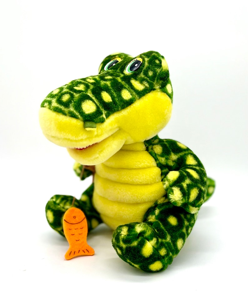 May include: Green and yellow plush alligator toy holding an orange fish. The alligator has a spotted pattern and large eyes.