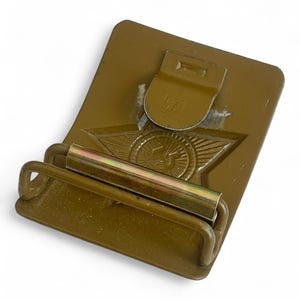 May include: Olive drab metal belt buckle with a star and wing emblem. The buckle has a rectangular base with a hinged clasp and a roller bar. The emblem features a star with wings and a circular design in the center.