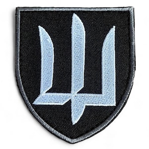 Op de afbeelding: Een zwarte geborduurde patch met een wit Oekraïens drietandsymbool in het midden. De patch heeft de vorm van een schild met een grijze rand.