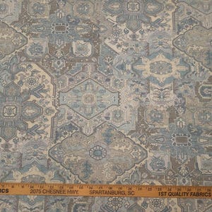 May include: Fabric with a repeating geometric pattern in shades of blue, beige, and brown. The design features stylized floral and geometric shapes. A wooden ruler is at the bottom with text.