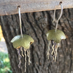 May include: A pair of silver dangle earrings with a green, textured, jellyfish design.