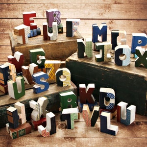 May include: A collection of alphabet letters made from repurposed books. The letters are arranged in a random order and are made from different colored book covers. The letters are all different sizes and shapes.