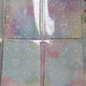 May include: Four clear plastic pockets with a white heart pattern. The pockets are designed to hold cards or other small items.