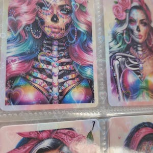 May include: A set of three colorful cards featuring a Day of the Dead theme. Each card has a woman with a sugar skull makeup design, flowers, and a rainbow background. The cards are numbered 5 and 7.
