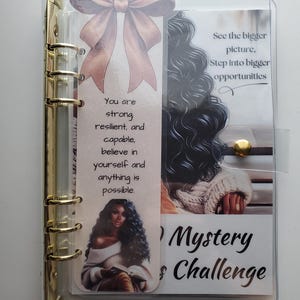 May include: A clear, gold-ringed binder with inserts. A bookmark with a bow and text that reads "You are strong, resilient, and capable, believe in yourself and anything is possible." Another insert reads "See the bigger picture, Step into bigger opportunities."