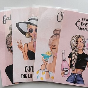 May include: Four pink and white cards with illustrations of women and text. The first card says "balance the little things". The second card says "Cheers to the good times". The third card says "Enjoy every moment". The fourth card says "Babe".