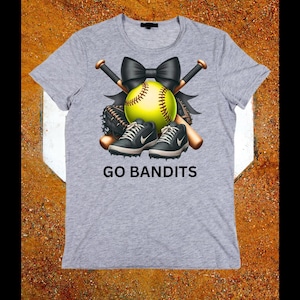 May include: A gray t-shirt featuring a softball design. The design includes a yellow softball, black bow, crossed baseball bats, a baseball glove, and black and gray sneakers. The text "GO BANDITS" is printed below the design.