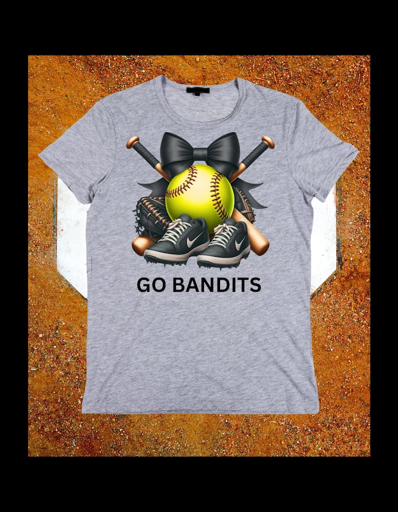 May include: A gray t-shirt featuring a softball design. The design includes a yellow softball, black bow, crossed baseball bats, a baseball glove, and black and gray sneakers. The text "GO BANDITS" is printed below the design.