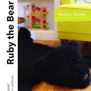 Puede incluir: Una alfombra de oso de piel sintética y franela negra con el texto "Ruby the Bear Rug" y "Modern Textiles" en la imagen.