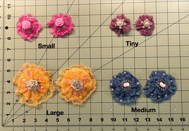 Pu&ograve; includere: Quattro paia di fermagli per capelli a forma di fiore in tessuto di diverse dimensioni: minuscolo, piccolo, medio e grande. I fermagli sono in pizzo e hanno dettagli di perle. I fiori sono in tonalit&agrave; di rosa, giallo e blu.