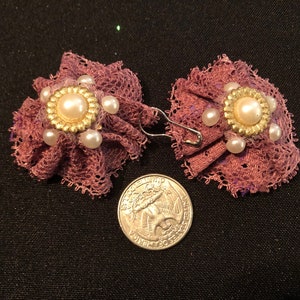 Pu&ograve; includere: Un paio di orecchini in pizzo viola con un accento di perla e oro. Gli orecchini sono circa delle dimensioni di una moneta da 25 centesimi.