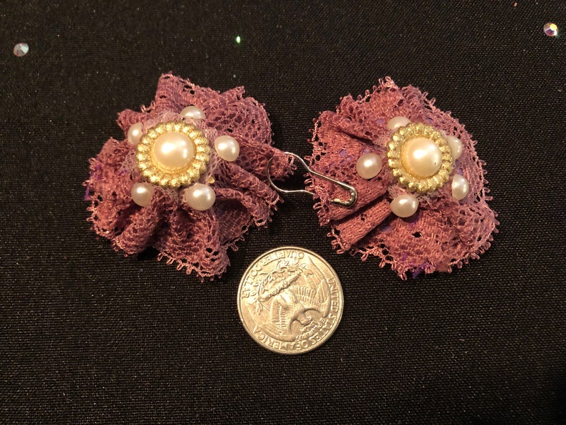 Pu&ograve; includere: Un paio di orecchini in pizzo viola con un accento di perla e oro. Gli orecchini sono circa delle dimensioni di una moneta da 25 centesimi.