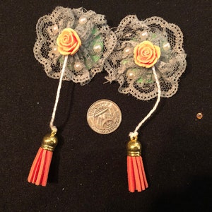 Pu&ograve; includere: Due decorazioni floreali in pizzo grigio con rose in tessuto color pesca e perline bianche. Ogni fiore ha un filo bianco attaccato con un fiocco dorato all'estremit&agrave;. I fiocchi sono rossi.