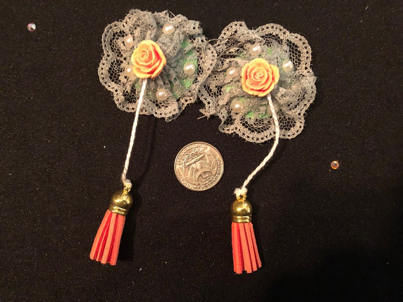 Pu&ograve; includere: Due decorazioni floreali in pizzo grigio con rose in tessuto color pesca e perline bianche. Ogni fiore ha un filo bianco attaccato con un fiocco dorato all'estremit&agrave;. I fiocchi sono rossi.