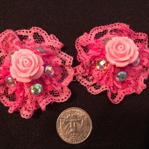 Pu&ograve; includere: Un paio di orecchini in pizzo rosa con una rosa rosa e strass. Gli orecchini sono circa delle dimensioni di una moneta da 25 centesimi.
