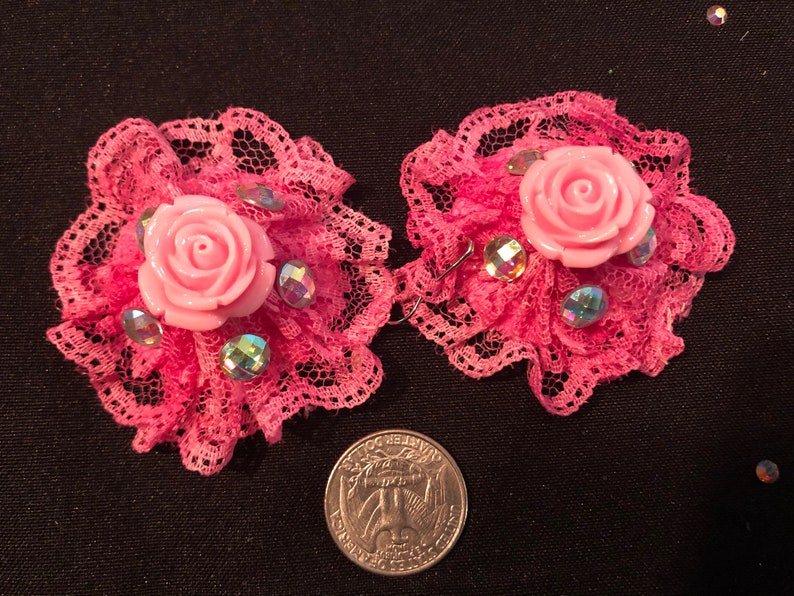 Pu&ograve; includere: Un paio di orecchini in pizzo rosa con una rosa rosa e strass. Gli orecchini sono circa delle dimensioni di una moneta da 25 centesimi.