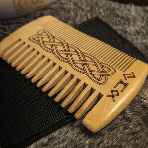 May include: A wooden comb with a Celtic knot design and runes. The comb is brown and has a black leather case.