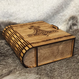 Op de afbeelding: Een houten doos met een scharnierend deksel, met een lasergegraveerd ontwerp van een hamer met ingewikkelde patronen. De doos is gemaakt van lichtbruin hout en heeft een natuurlijke afwerking.