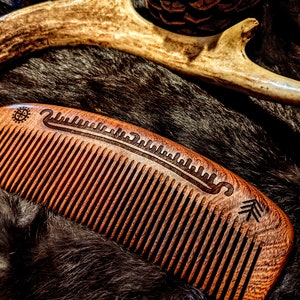 May include: A wooden comb with a carved design on the back. The comb is brown and has a natural finish. It is lying on a brown fur surface.