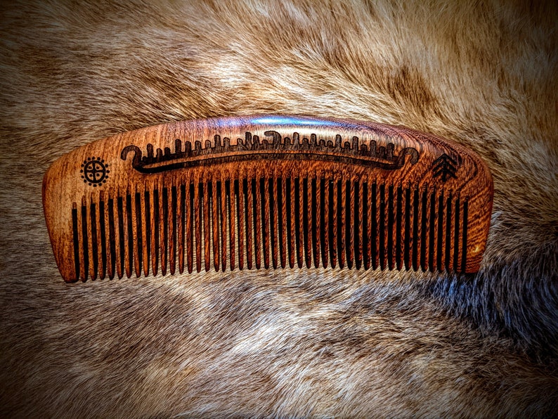 May include: A wooden comb with a dark brown finish and a carved design on the top. The comb has fine teeth and is curved.