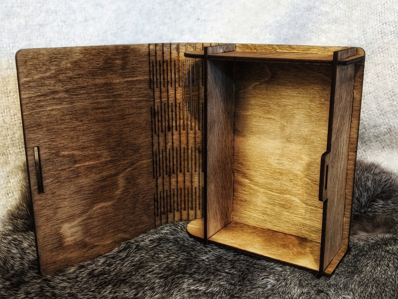 Op de afbeelding: Een houten doos met een scharnierend deksel dat opengaat om een ​​lege binnenkant te onthullen. De doos is gemaakt van donkerbruin hout en heeft een natuurlijke houten afwerking.