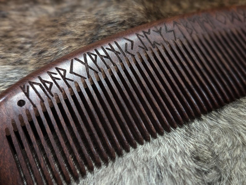 May include: A dark brown wooden comb with a row of teeth and runes carved into the top. The comb is lying on a light brown furry surface.