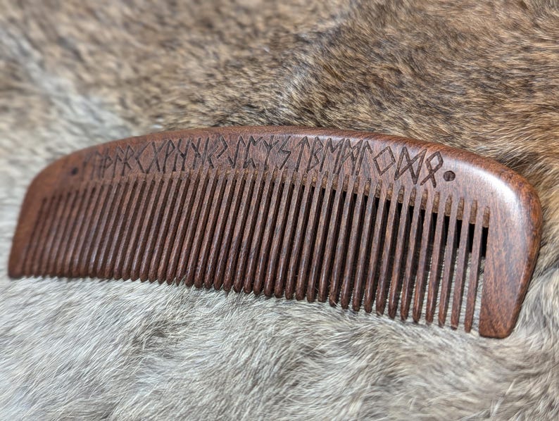 May include: A dark brown wooden comb with a row of teeth and a carved design of runes on the top.