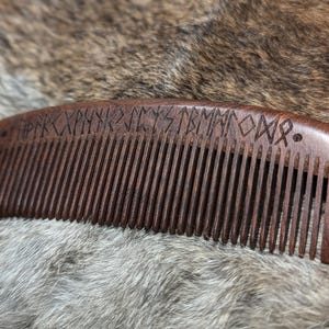 May include: A dark brown wooden comb with a row of teeth and a carved design of runes on the top.