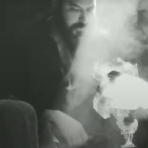 May include: A close-up of a person's face with a beard, obscured by smoke or steam. The person is wearing a dark shirt and is looking at something off-camera.