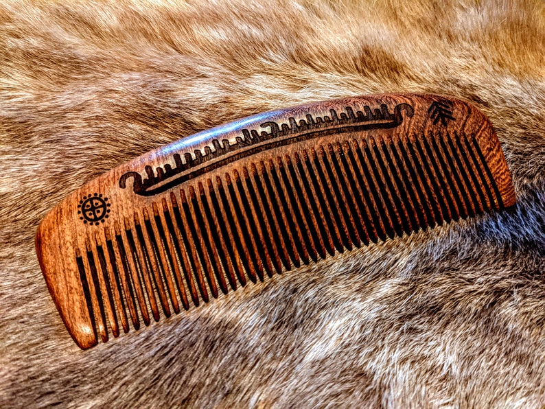 May include: A wooden comb with a carved design of a boat and a compass. The comb is brown and has a natural finish.