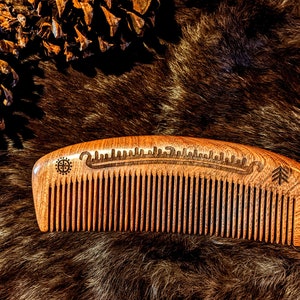 May include: A wooden comb with a carved design and a tree symbol. The comb is brown and has a curved shape.