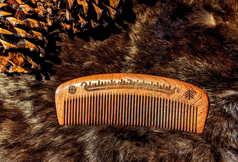 May include: A wooden comb with a carved design and a tree symbol. The comb is brown and has a curved shape.
