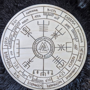 May include: A wooden circular calendar with Norse runes and symbols. The calendar features the months of the year in English and Norse, along with the names of the Norse holidays. The calendar is divided into four sections representing the seasons: winter, spring, summer, and fall.