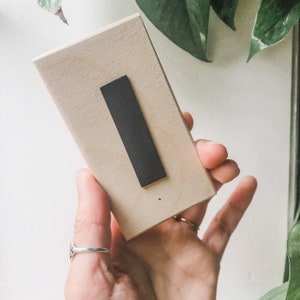 Puede incluir: La parte posterior de un letrero de madera con una tira magn&eacute;tica negra adherida. El letrero es de color marr&oacute;n claro y tiene una superficie lisa.