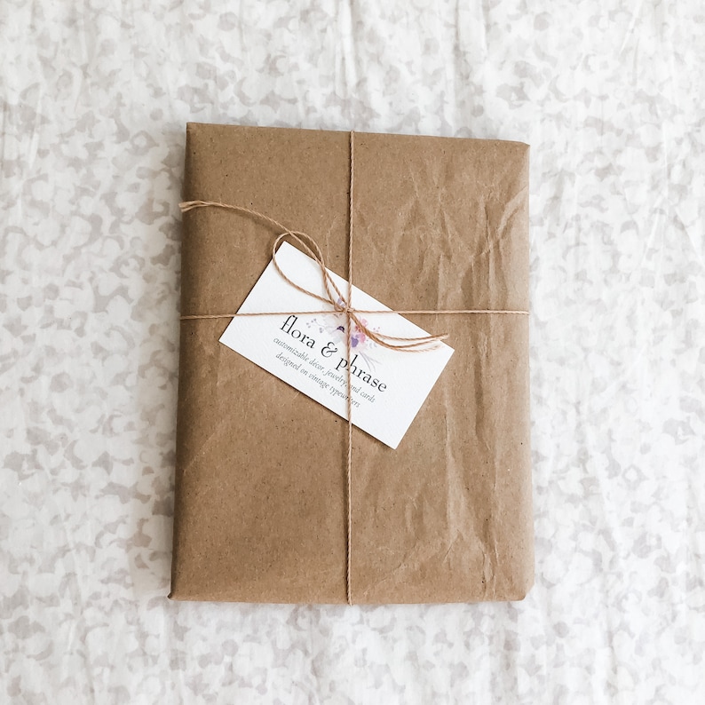 May include: A brown paper package tied with twine and a business card that reads "flora & phrase, customizable decor, jewelry, and finds, designed in vintage spirit."