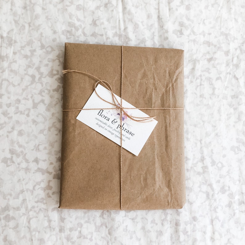 May include: A brown paper package tied with twine and a business card that reads "flora & phrase, customizable decor, jewelry, and finds, designed in vintage spirit."