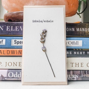May include: A white card with the text "inhale/exhale" printed on it. A dried lavender flower is attached to the card.