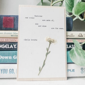 K&ouml;nnte beinhalten: Eine wei&szlig;e Karte mit einem Zitat von Emily Bront&euml;. Das Zitat lautet: "Whatever our souls are made of, his and mine are the same." Eine gepresste wei&szlig;e Blume ist auf die Karte geklebt.