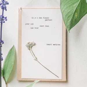 Könnte beinhalten: Ein gerahmter Druck mit einer gepressten Blume und einem Gedicht in Französisch von Henri Matisse. Das Gedicht lautet: "il y a des fleurs partout pour qui veut bien les voir".