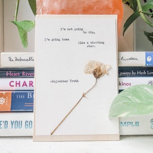 May include: A white wooden sign with a pressed flower and a quote by Sojourner Truth: "I'm not going to die, I'm going home like a shooting star."